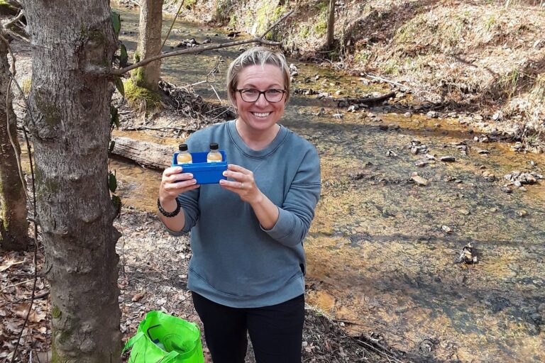 Volunteer holding up a water testing kit beside a creek.