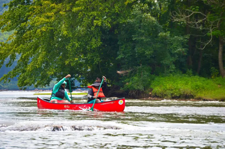 two men life jackets paddle a red canoe down the river.