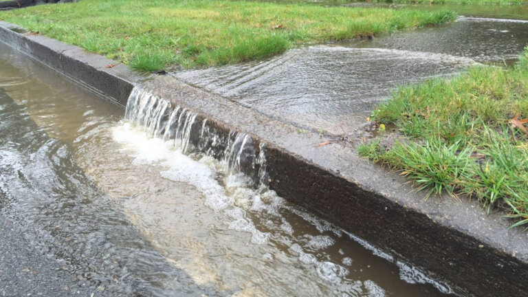 Storm water runoff draining off lawn and sidewalk and running down a street curb.