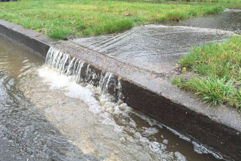 Storm water runoff draining off lawn and sidewalk and running down a street curb.